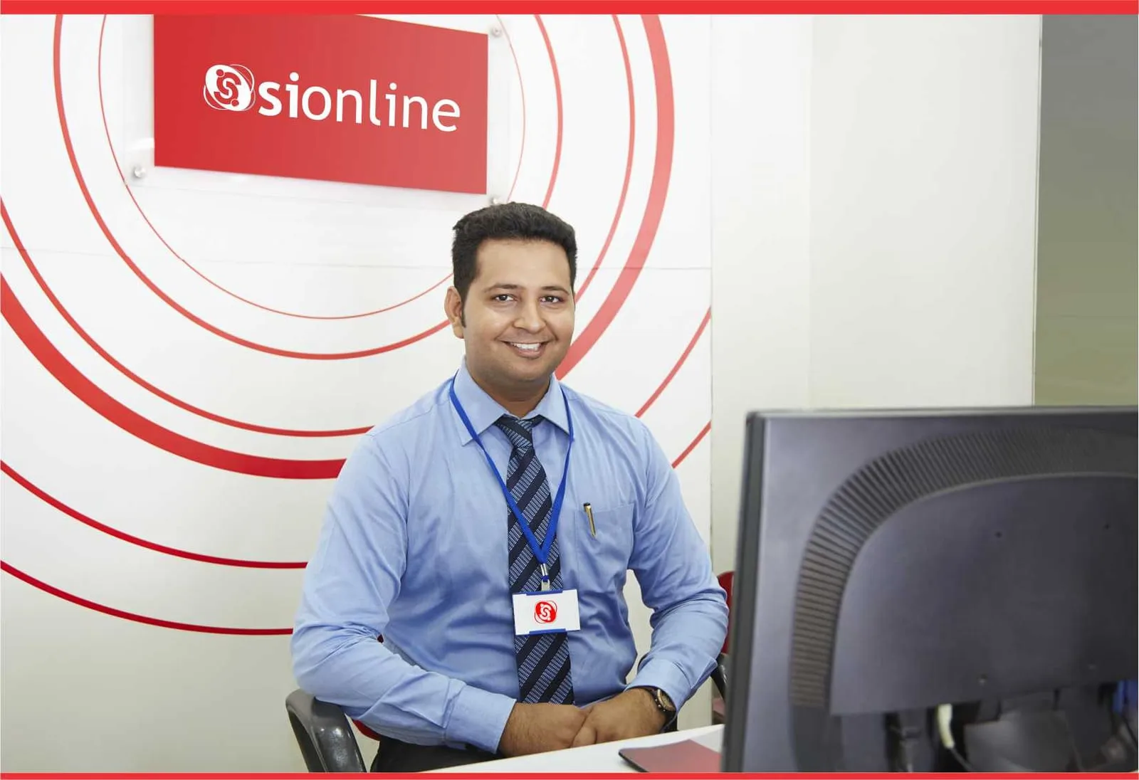 A SiOnline team member seated at a desk in front of the SiOnline logo wall